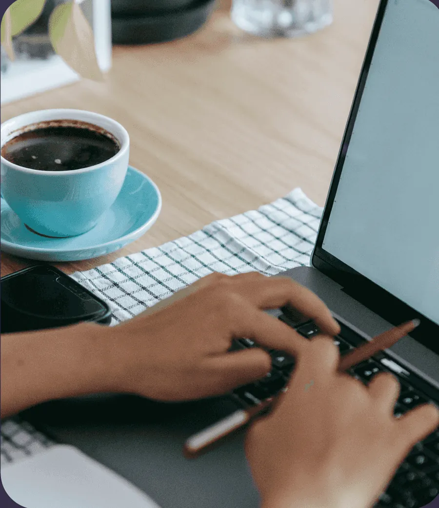 Hands typing on a laptop next to a cup of coffee